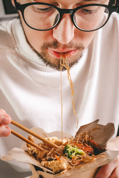 Çin yemeği yiyen bir adam. Eve teslim. Deniz mahsullü erişte. Sebzeli. Asya yemeği - Fotoğraf, Görsel
