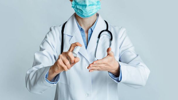 Έννοια απολύμανσης. Γιατρός με προστατευτική μάσκα τρίβει τα χέρια με αντισηπτικό - Φωτογραφία, εικόνα