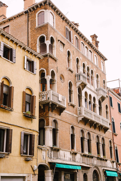 Closeup of the facade of a building, on the streets of Venice, Italy. Five-story stone building with white balconies with columns, classic Venetian arched windows. - Фото, изображение