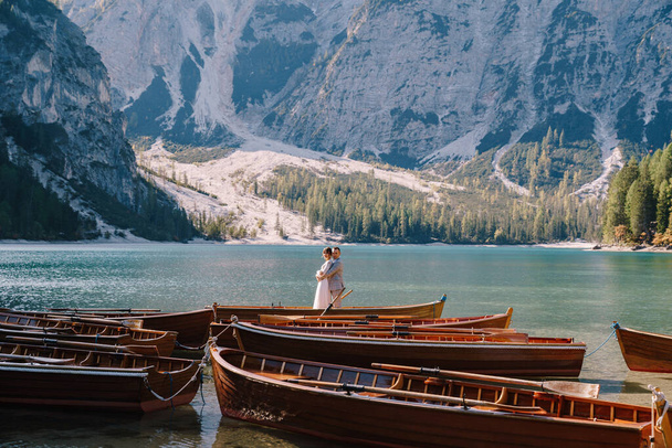 Bride and groom sailing in wooden boat, with oars at Lago di Braies lake in Italy. Wedding in Europe - Newlyweds are standing embracing in a boat. - Photo, Image