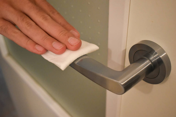 Рука знезаражує вологою тканиною ручку дверей будинку як запобігання бактерій, вірусів і мікробів
 - Фото, зображення