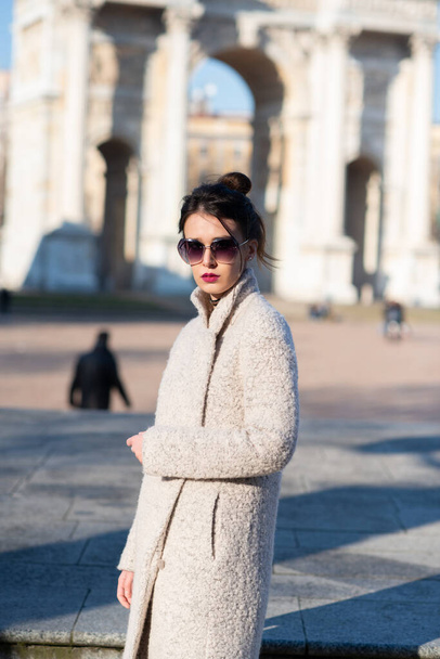 Jolie jeune femme portant un manteau gris avec de longs cheveux foncés et des lunettes de soleil posant en plein air dans les rues de Milan, en Italie. Beau portrait de modèle caucasien. Mode Steet - Photo, image
