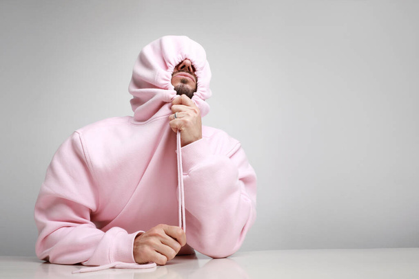 Crazy and happy Image of young man wearing pink hoodie over white background. Horizontal. - 写真・画像