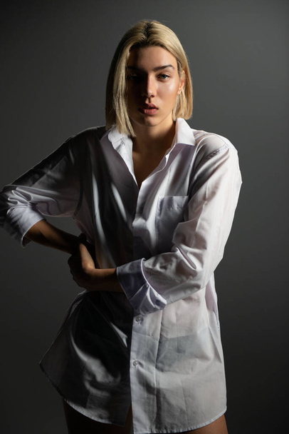 Fashion model. Young blond woman posing in studio wearing white shirt. Beautiful caucasian girl over gray background - Fotó, kép