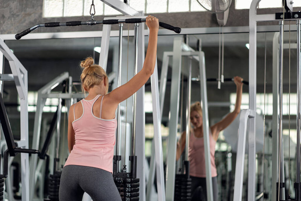 Strong young woman exercising with pulldown machine in a fitness club, doing exercises in gym - Foto, Imagem
