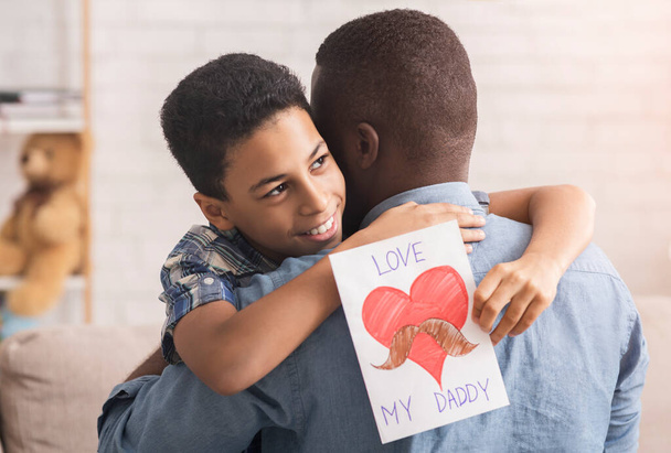Pieni afro poika halaa isää ja antaa hänelle käsintehty postikortti
 - Valokuva, kuva