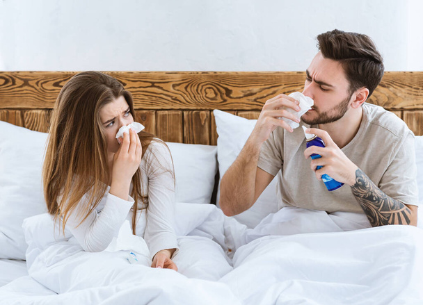 Κρύο και γρίπη μαζί έννοια. Σύζυγος και γυναίκα στο κρεβάτι σκουπίστε τη μύτη με πετσέτα - Φωτογραφία, εικόνα