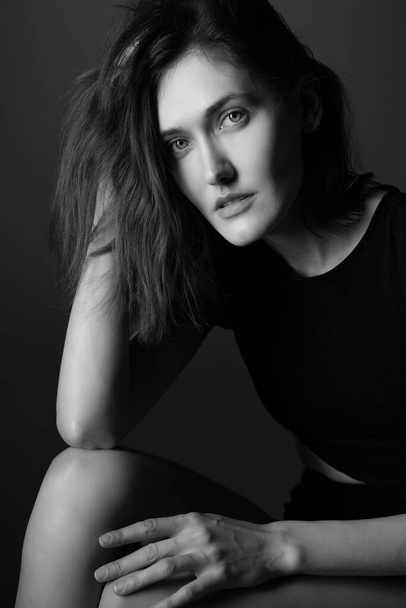 Fashion model. Portrait of young woman posing in studio wearing black drees. Beautiful caucasian girl over gray background. Black and white - Fotografie, Obrázek