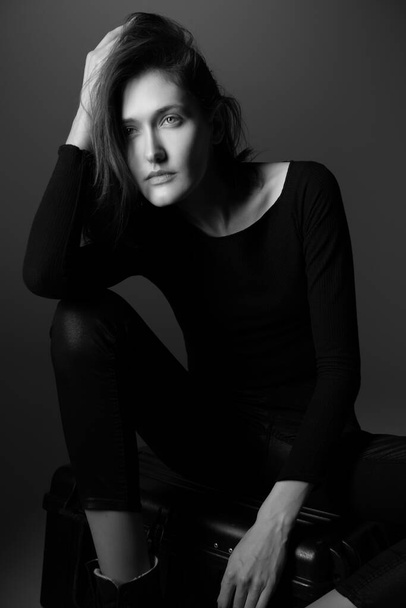Fashion model. Young woman posing in studio wearing black with boots. Beautiful caucasian girl over gray background. Black and white - Φωτογραφία, εικόνα