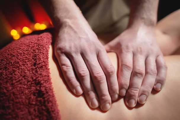 Close-up male hands of a professional massage therapist make professional anti-cellulite massage to a female client in a specialized salon in a dark room - Фото, зображення
