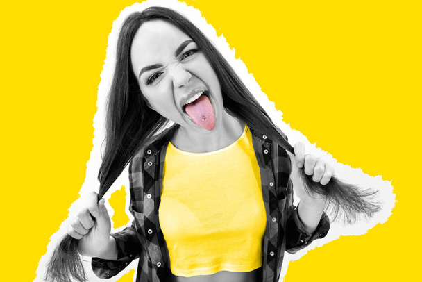 Hipster girl in checked shirt showing tongue with piercing over yellow background. Impertinent behaviour. Hipsters. Provocation. Aggression. Naughtiness. High fashion - 写真・画像