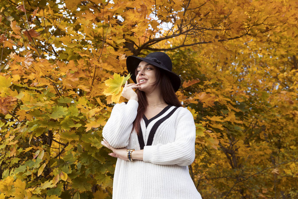 Rudowłosy dziewczyna w białym swetrze i czarny kapelusz pozowanie w jesiennym lesie - Zdjęcie, obraz