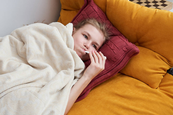ziek tiener liggend in bed met behulp van thermometer - Foto, afbeelding
