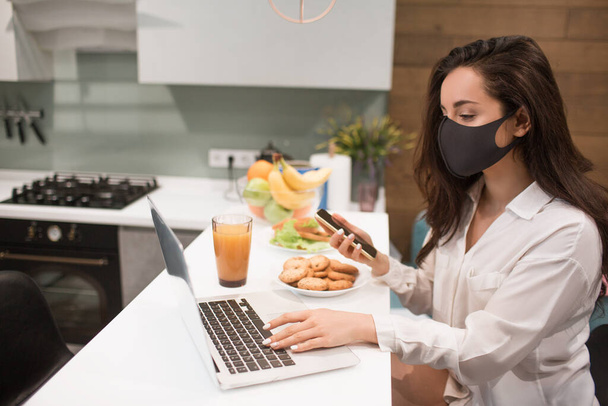 Debido a la pandemia del coronavirus, una mujer aislada en casa. Ella trabaja en casa, lleva una máscara y tiene una videoconferencia en su computadora portátil
. - Foto, imagen