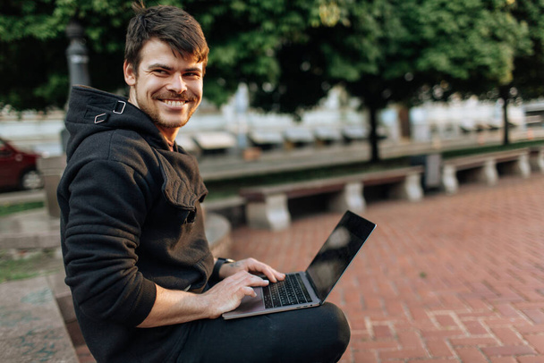 Młody mężczyzna pracuje na laptopie w centrum miasta. Niezależna osoba pisząca coś w swoim dokumencie. czatowanie z przyjaciółmi przez internet, kamerki internetowe - Zdjęcie, obraz
