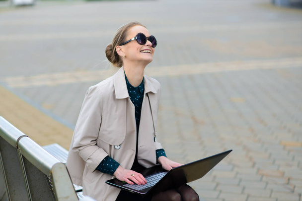Young beautiful businesswoman with sunglasses, phone, laptop, cup of coffee in the city street - Foto, Imagem