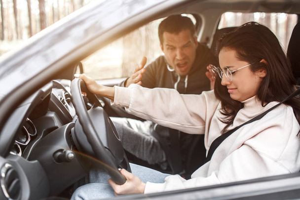 Driving instruction. A young woman learns to drive a car for the first time. She does not work well. Her husband or instructor yells at her. She is crying - Photo, Image
