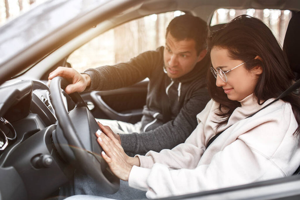 Driving instruction. A young woman learns to drive a car for the first time. She does not work well. Her husband or instructor yells at her. She is crying - Zdjęcie, obraz