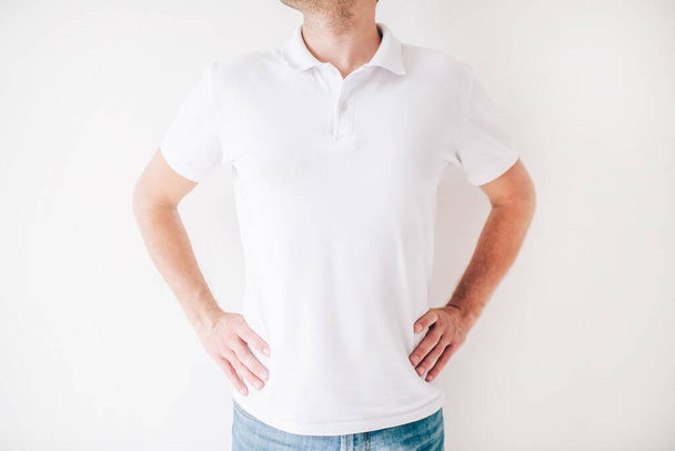 Young man isolated over white background. Cut view of guy stand alone in studio and hold hands on hips. Wear white shirt. - Photo, Image