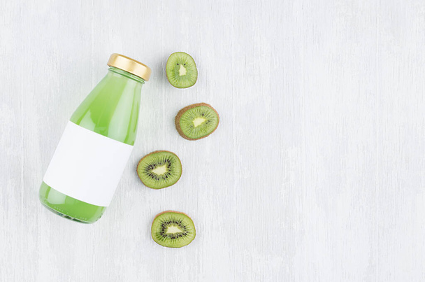 Bright green kiwi juice in glass bottle with blank label, sliced fruit on white wooden board, top view, copy space, template for design, advertising, portfolio. - Foto, afbeelding