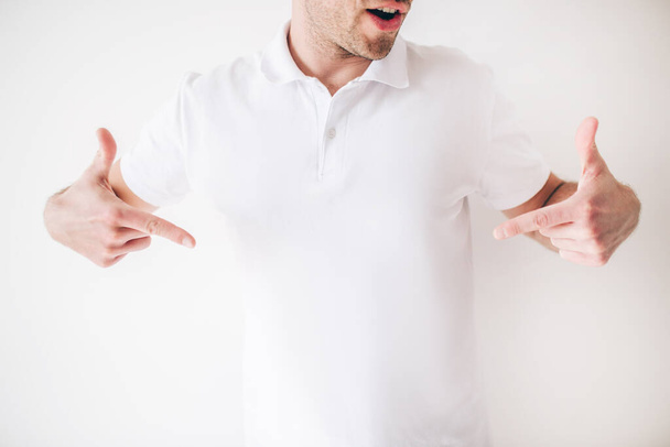 Young man isolated over white background. Cut view of cool confident male person point down with both hands fingers. Guy in white shirt in studio alone. - Photo, Image