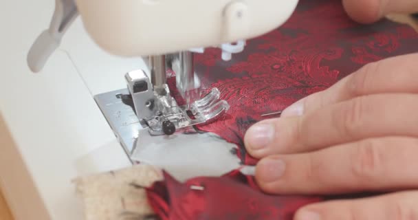 Belle main masculine pousse le matériau de doublure paisley rouge à travers une machine à coudre pendant le processus de fabrication de costume. Mode, création et couture. Vue grand angle
 - Séquence, vidéo