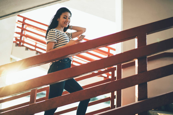Smiling female blogger climbing outdoors stairs and enjoying online communication with social followers, millennial Asian hipster girl searching online information on public wireless website - Fotoğraf, Görsel