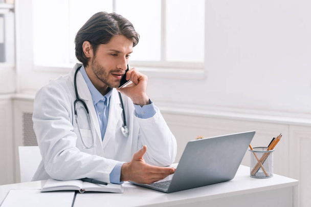 Poważny lekarz pracujący na laptopie i mający telefon - Zdjęcie, obraz