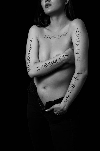 Siyah zemin üzerinde hakaret, zulüm, eşitsizlik yazan genç bir kadının vücudunun bir parçası. Fotoğraf. Yazı, fotoğrafçının elinde yazan bir dövme değil.. - Fotoğraf, Görsel