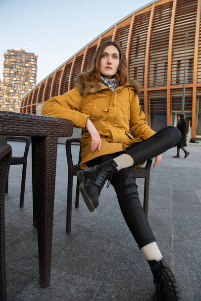 Modelo de moda sentado y posando al aire libre. Joven rubia caucásica posando al aire libre de invierno. Hermosa chica, retrato urbano en Milán, Italia - Foto, imagen