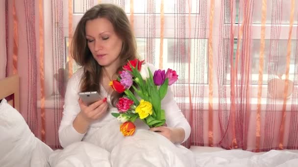 vrouw belt op slimme mobiele telefoon en bedankt voor het boeket van bloem tulpen. 4K - Video