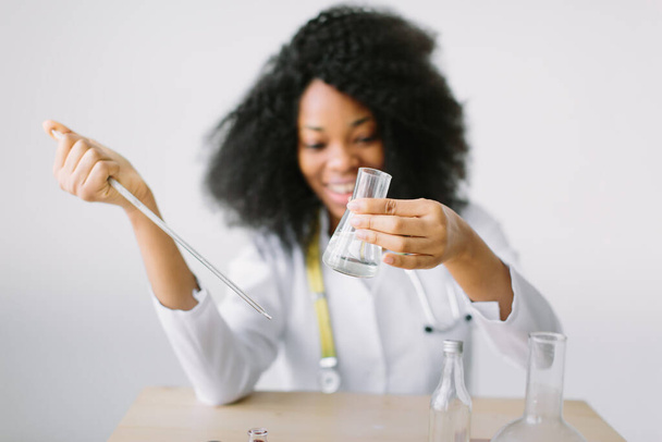 Νεαρή όμορφη Αφροαμερικανή γιατρός με λευκό παλτό και στηθοσκόπιο. κάθεται σε ένα τραπέζι και Αναλύοντας Δείγμα στο Laboratory.laboratory βοηθός αναλύοντας ένα δείγμα. - Φωτογραφία, εικόνα