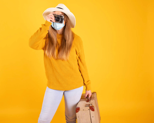 Девушка-туристка в медицинской маске, чемодане, шляпе-камере не может путешествовать по ковид-19
 - Фото, изображение