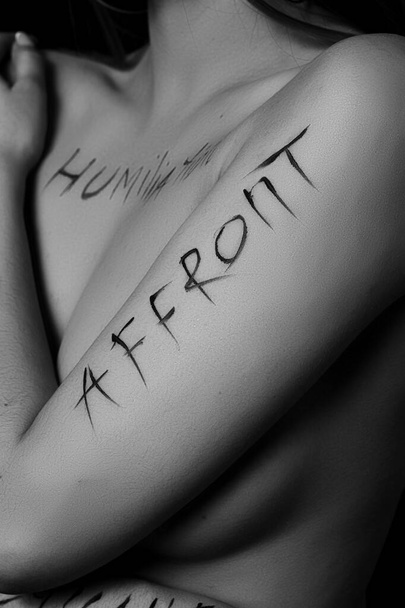 part of a young woman's body with the words affront,cruelty,inequality on a black background.photo.the inscription is not a tattoo, written by the photographer's hand. - Фото, зображення