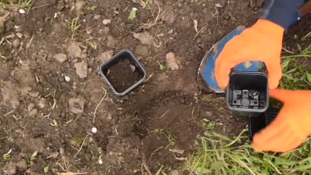 a man in the garden in orange gloves pours earth with a small shovel into a pot - Video
