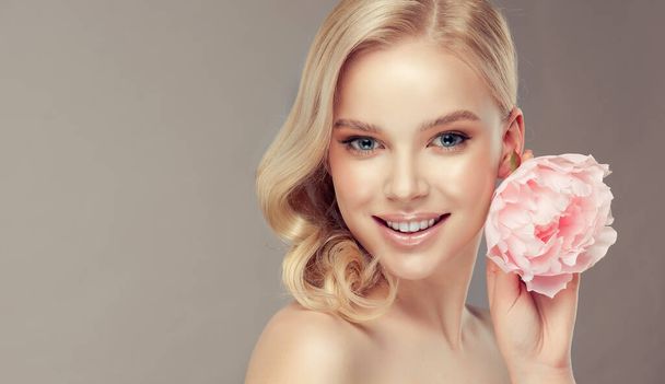 Beautiful young blonde woman with delicate peony flower. Girl clean fresh skin . Facial treatment . Cosmetology , beauty and spa . Face care - Foto, immagini