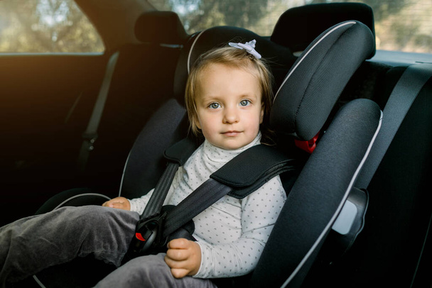 Transport, safety, childhood road trip and people concept. Happy Caucasian cute little baby girl sitting in baby car seat. Child in auto baby seat in car. Adorable little girl in the car. - Фото, изображение