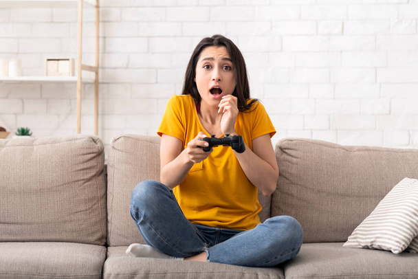 Емоційна дівчина тисячоліття з консоллю грає у відеоігри на затишному дивані вдома
 - Фото, зображення
