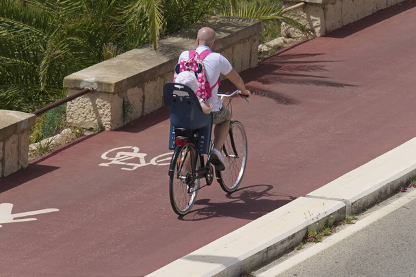 Italie ; Sicile, Marina di Ragusa (province de Ragusa), cycliste avec un enfant sur une piste cyclable avec des vélos signe
  - Photo, image