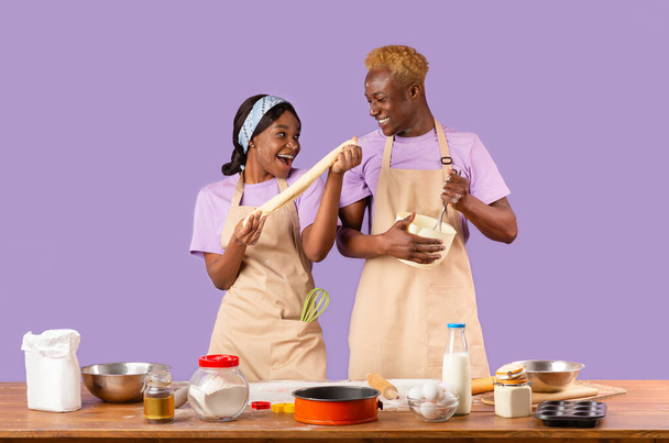 Молода чорна сім'я насолоджується процесом приготування їжі, проводячи вихідні разом на кольоровому фоні
 - Фото, зображення