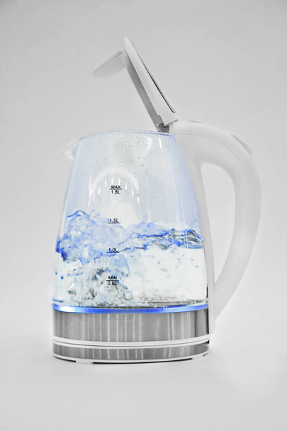                    El agua hierve en un hervidor eléctrico transparente sobre un fondo blanco. macro. pequeños electrodomésticos para el hogar y la cocina
.                                            - Foto, Imagen
