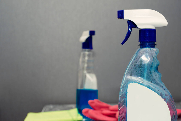 μπλε δοχείο με ψεκαστήρα για το πλύσιμο των παραθύρων και ροζ γάντι καουτσούκ σε ένα θολό φόντο - Φωτογραφία, εικόνα