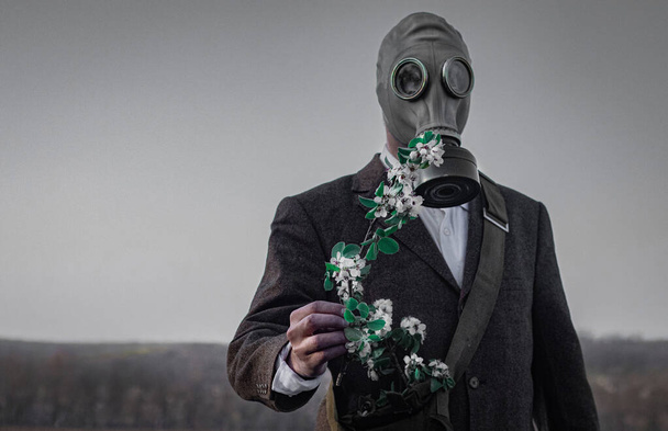 un homme dans un masque à gaz avec un arrosoir dans ses mains se tient sur un terrain vide près d'un seul arbre à fleurs
 - Photo, image