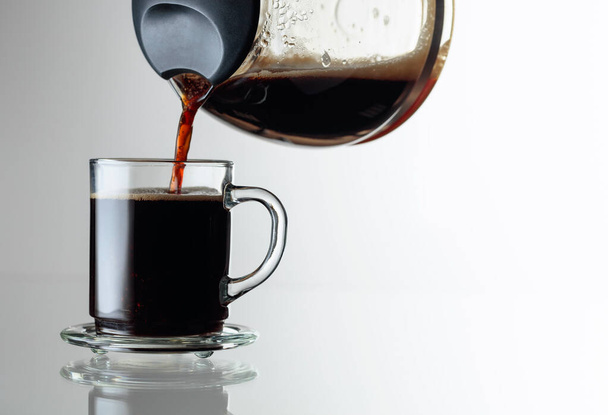 Czarna kawa w szklanym kubku na szklanym stole. Kawa jest przelewana z ekspresu do kawy do filiżanki. Przestrzeń kopiowania. - Zdjęcie, obraz