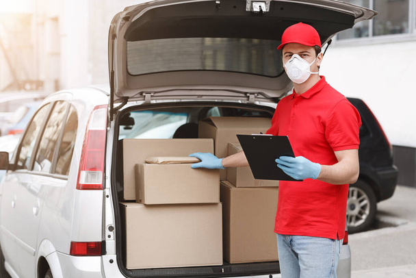 Delivery man is checking parcel. Courier with tablet, put his hand on box in car - 写真・画像