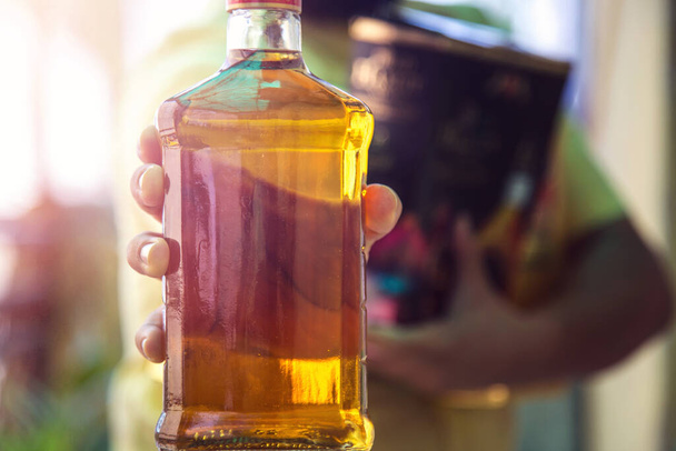 Großaufnahme der Hand eines Kunden, der die Whisky-Schnapsflasche zeigt, als er nach dem Kauf von Schnaps in einem Geschäft inmitten der andauernden Covid-19-Sperrung geht - Foto, Bild