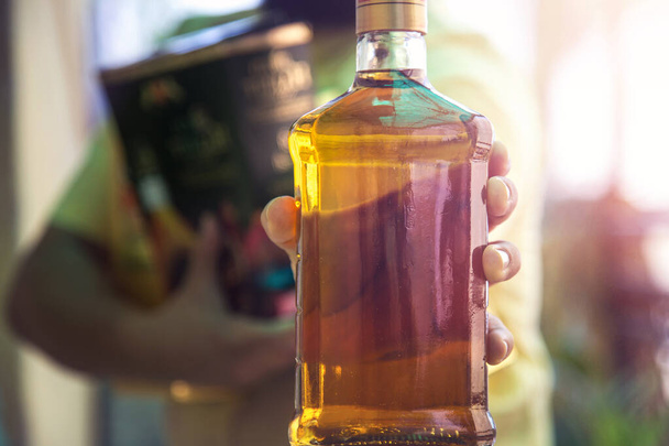 Primer plano de la mano del cliente mostrando la botella de licor de whisky al salir después de comprar licor en una tienda en medio del bloqueo continuo de Covid-19
 - Foto, imagen