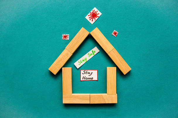 Huis gemaakt van houten blokken met de inscriptie "blijf veilig, blijf thuis" binnen en covid-19 buiten op een blauwe achtergrond. Concept van hoe het coronavirus te stoppen. Vlakke lay, bovenaanzicht, kopieerruimte. - Foto, afbeelding