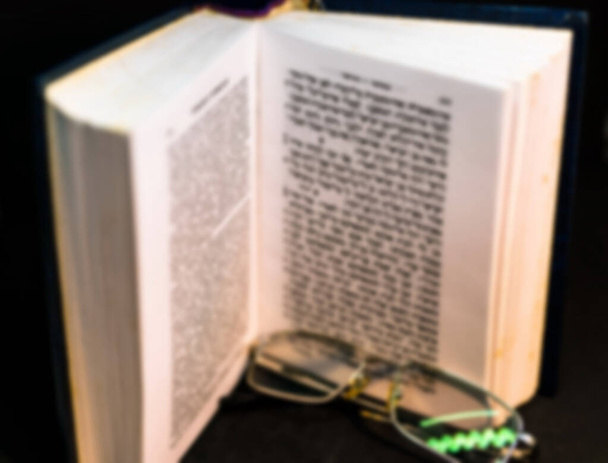 Offenes Talmud-Thora-Tanach-Buch auf schwarzem Hintergrund mit Brille. Selektiver Fokus. Verschwommene Sicht - Foto, Bild