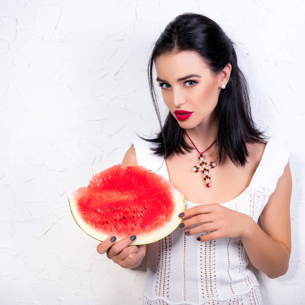 Beautiful young woman holding and eating slice of ripe red fresh juicy tasty sweet watermelon - 写真・画像